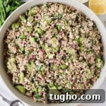 Tuna cucumber salad in a bowl with parsley, feta, lemon and honey in a jar on the sides.