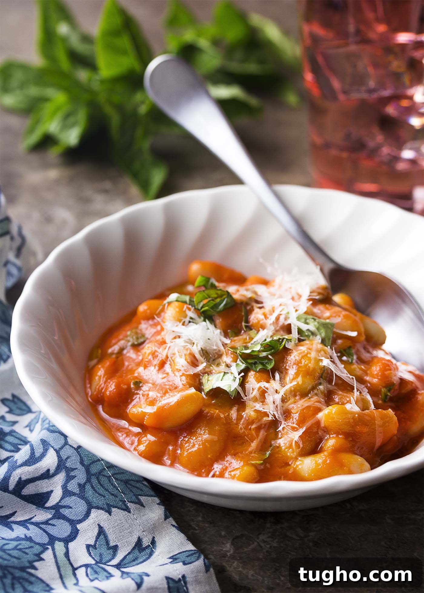 White bowl with a spoon. Bowl full of creamy white beans and pomodoro sauce topped by parmesan and herbs.