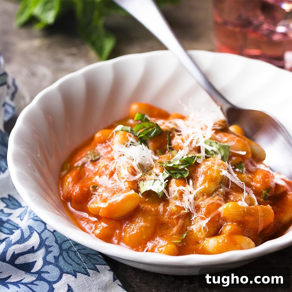 A white bowl of beans in pomodoro sauce topped by cheese and herbs.