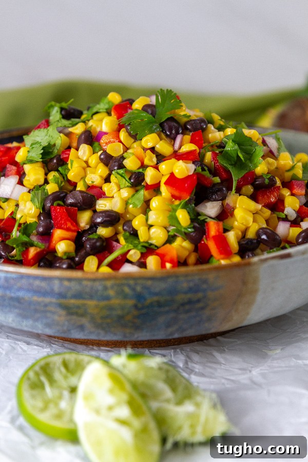 a blue bowl filled with corn, black beans, red pepper, and cilantro with squeezed lime wedges next to it.