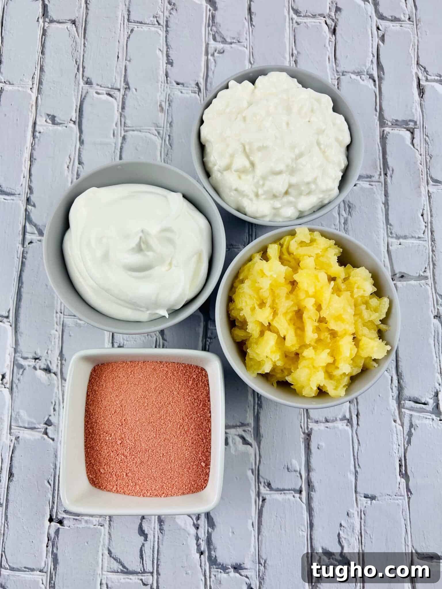 Four bowls containing yogurt, cottage cheese, crushed pineapple, and a vibrant mix for a Cottage Cheese arranged on a white brick-patterned surface.