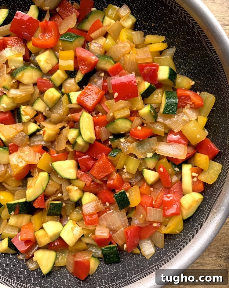 Beef and Pepper Rice Bowls 6 Close up view of sautéed chopped onion, red bell pepper, yellow bell pepper, and zucchini in a pan with chopped garlic.