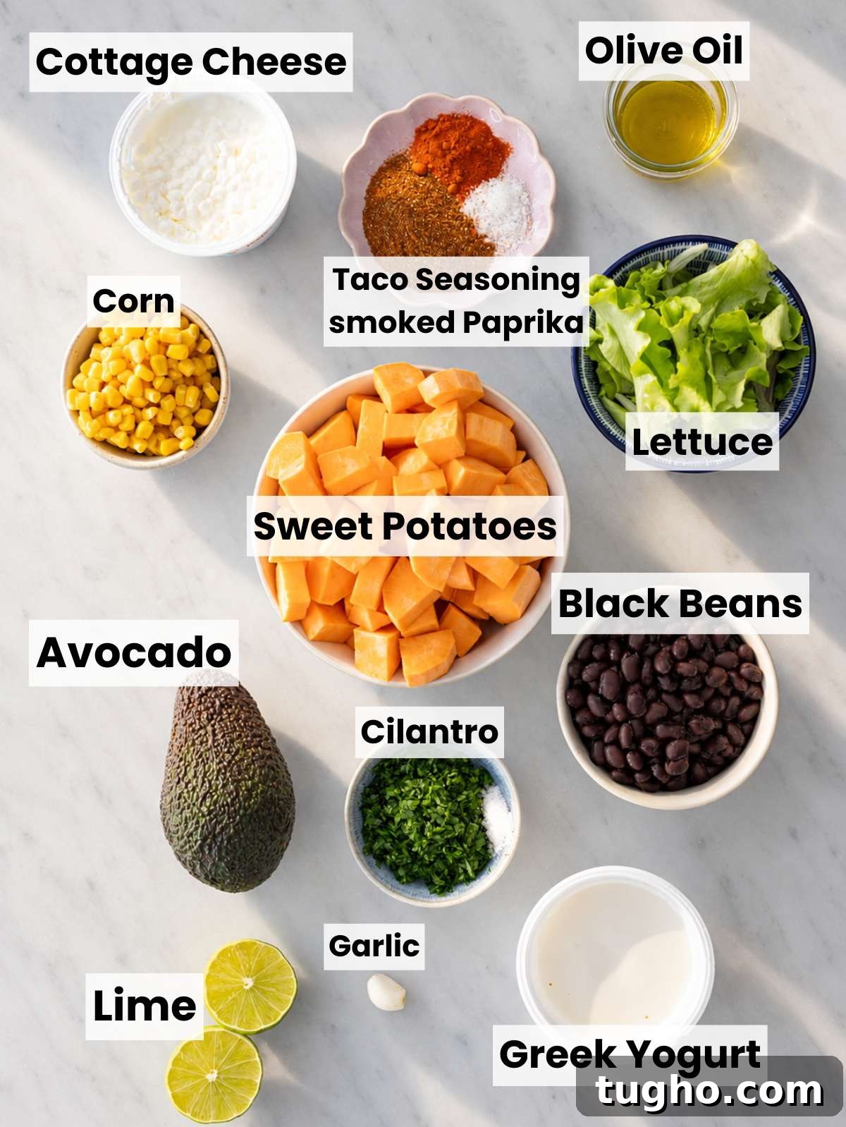 Sweet potatoes, black beans, lettuce, avocado, lime, and spices on a marble countertop.