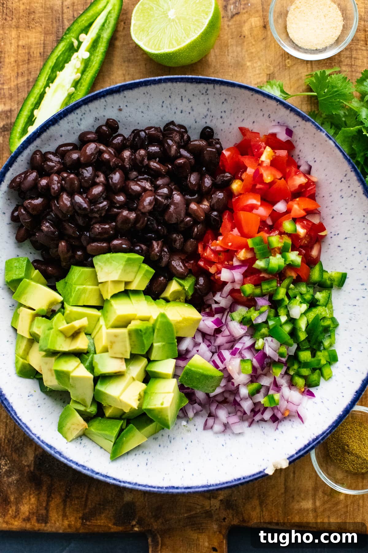Bowl with black bean salsa ingredients in it on wooden cutting board.