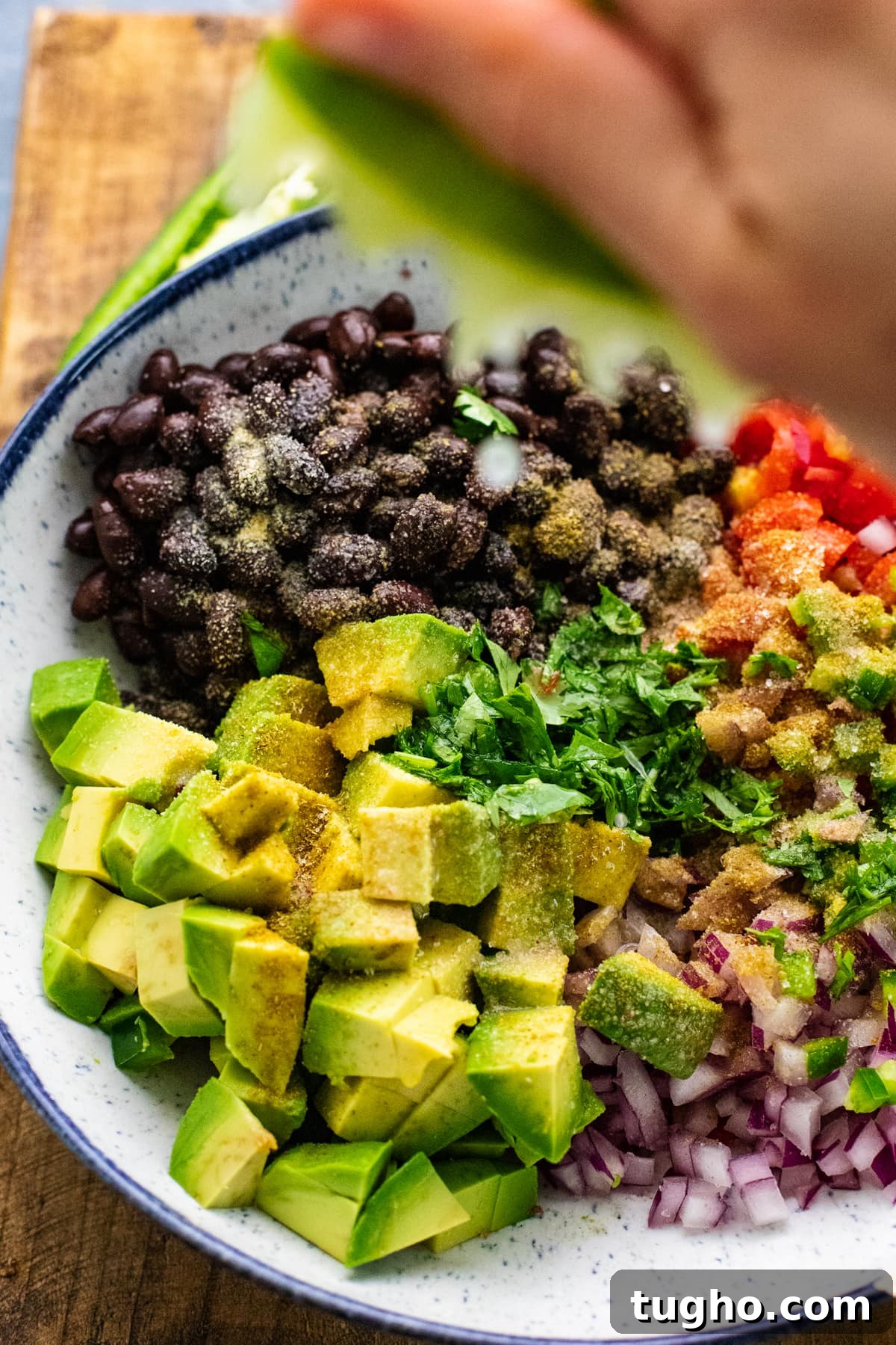 hand squeezing lime over bowl with black bean salsa ingredients in it.