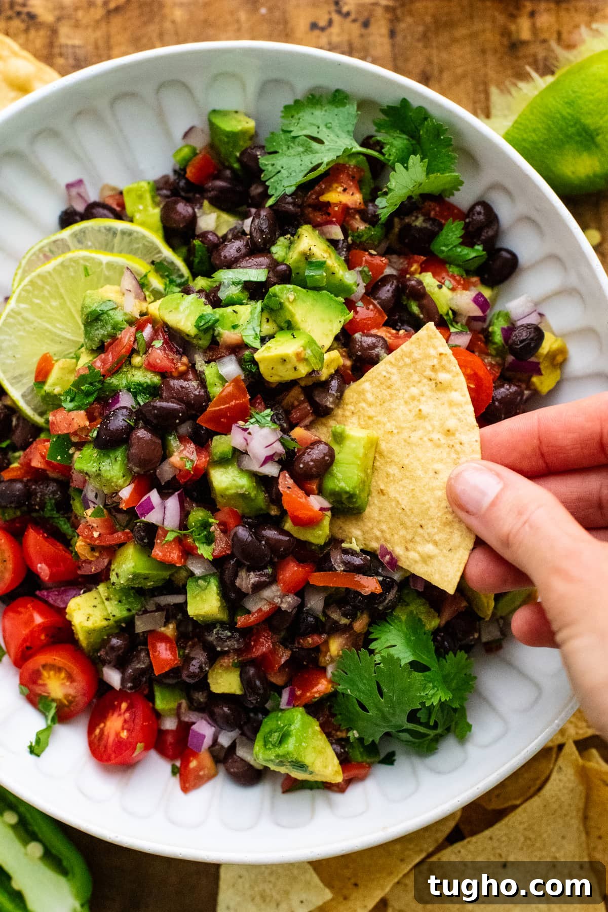 hand dipping chip into black bean salsa in white bowl.