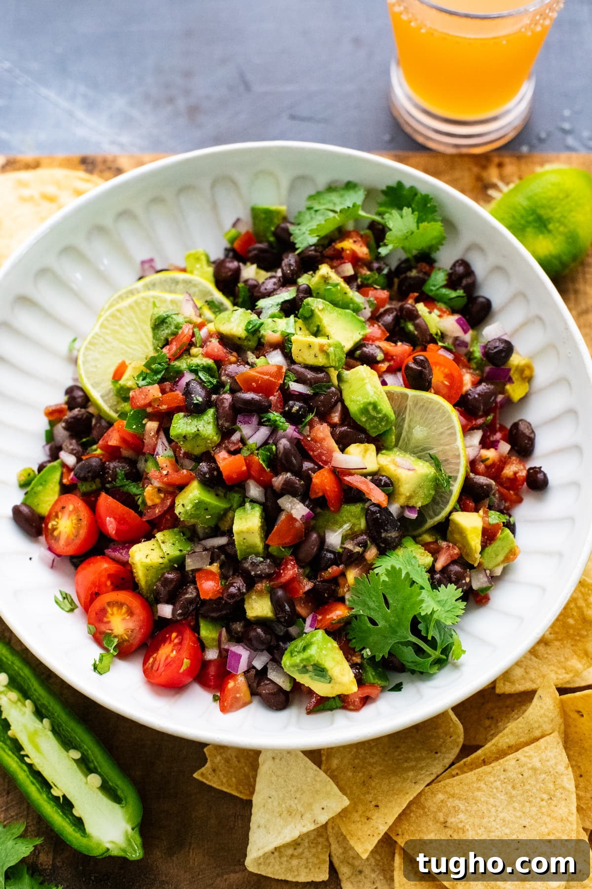 White bowl with black bean salsa in it with lime slices and tortilla chips arranged around it.