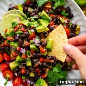 hand dipping chip into black bean salsa in white bowl.