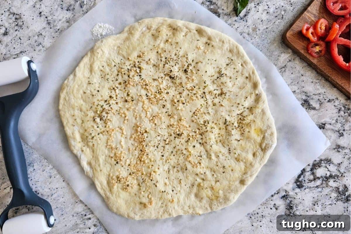 pizza dough rolled out on parchment paper and topped with olive oil, minced garlic and oregano.