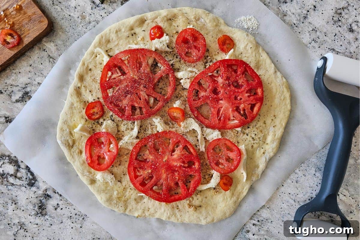 Pizza dough with olive oil, seasonings, fresh mozzarella cheese and parmesan cheese that is topped with fresh tomatoes before baking.
