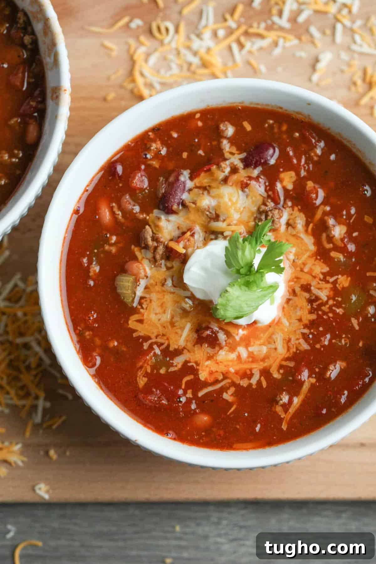 Freezer Meals for Large and Small Families 2 A bowl of chili topped with shredded cheese, a dollop of sour cream, and a sprig of cilantro, with scattered cheese on the wooden surface nearby.