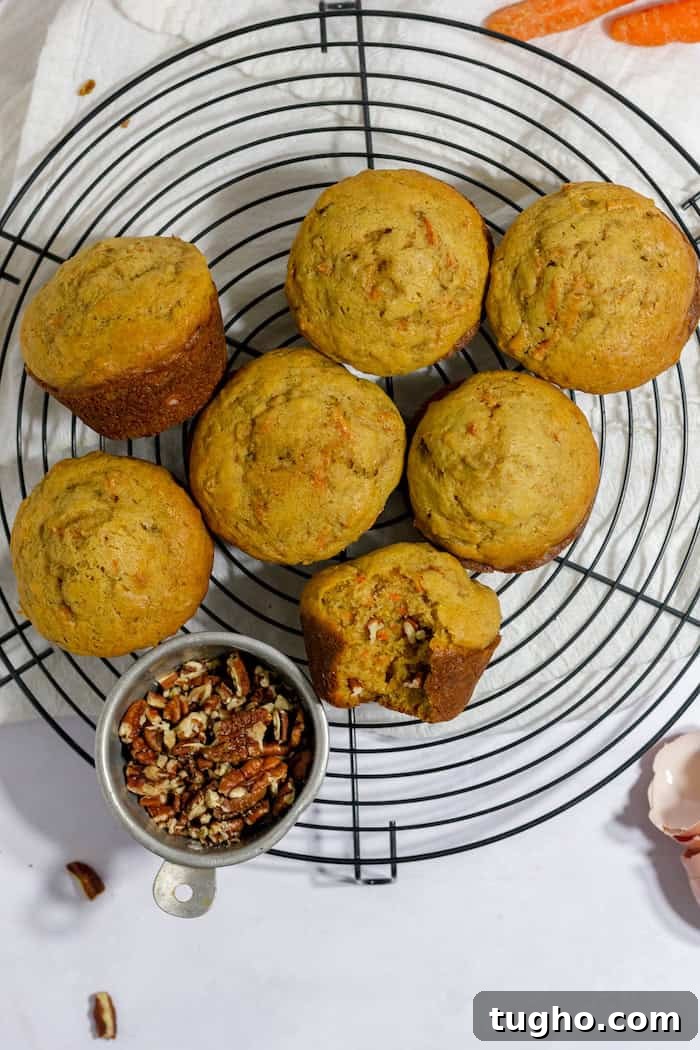 Moist Gluten-Free Carrot Muffins 2 Photo, taken from above, shows seven gluten free carrot muffins on a wire trivet. One muffin has a bite taken out of it, and a small bowl of walnuts sits nearby.