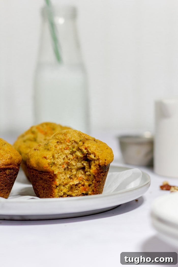 Moist Gluten-Free Carrot Muffins 4 Photo shows three gluten free carrot muffins sitting on a white plate in a white kitchen. Front muffin has a bite taken out of it.