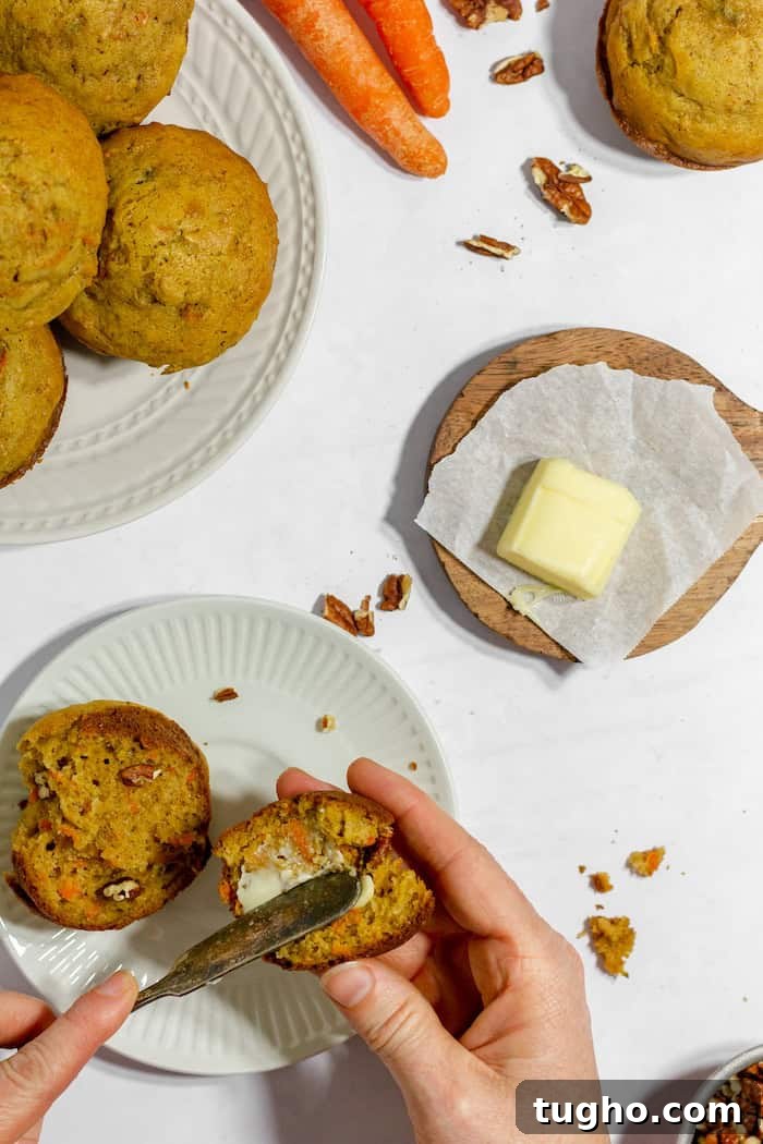Moist Gluten-Free Carrot Muffins 5 Image, taken from above shows a woman's hands spreading butter onto a gluten free carrot muffin. Nearby sits a wooden plate with more butter, and a white plate filled with more muffins.