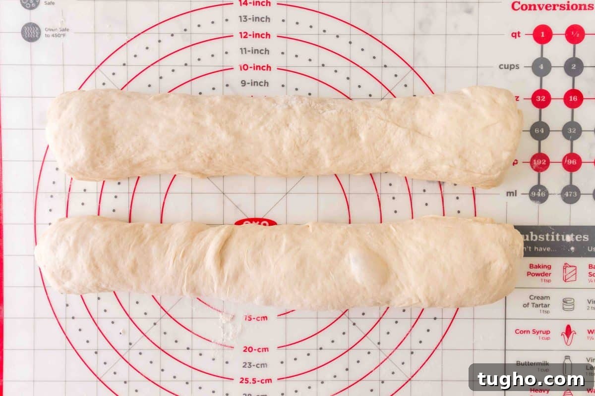 French Baguette Recipe: Make Two Loaves at Home 11 Two baguettes of French bread dough rolled into baguette log shapes on a pastry mat. Hostess At Heart