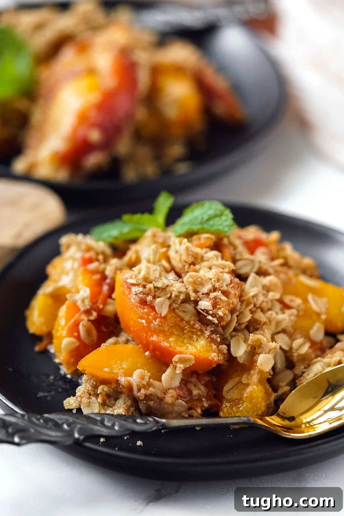 Oat-Topped Peach Crumble Recipe 2 Baked peach crisp or crumble with oats served in small dessert plates garnished with mint leaves.
