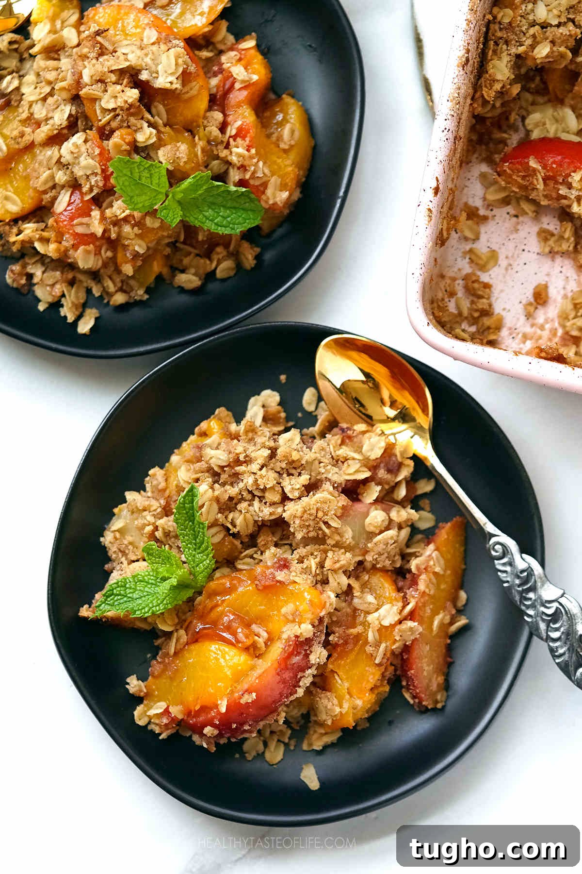 Oat-Topped Peach Crumble Recipe 7 Overhead shot of baked peach crumble with oats served on a dessert plate with a spoon.