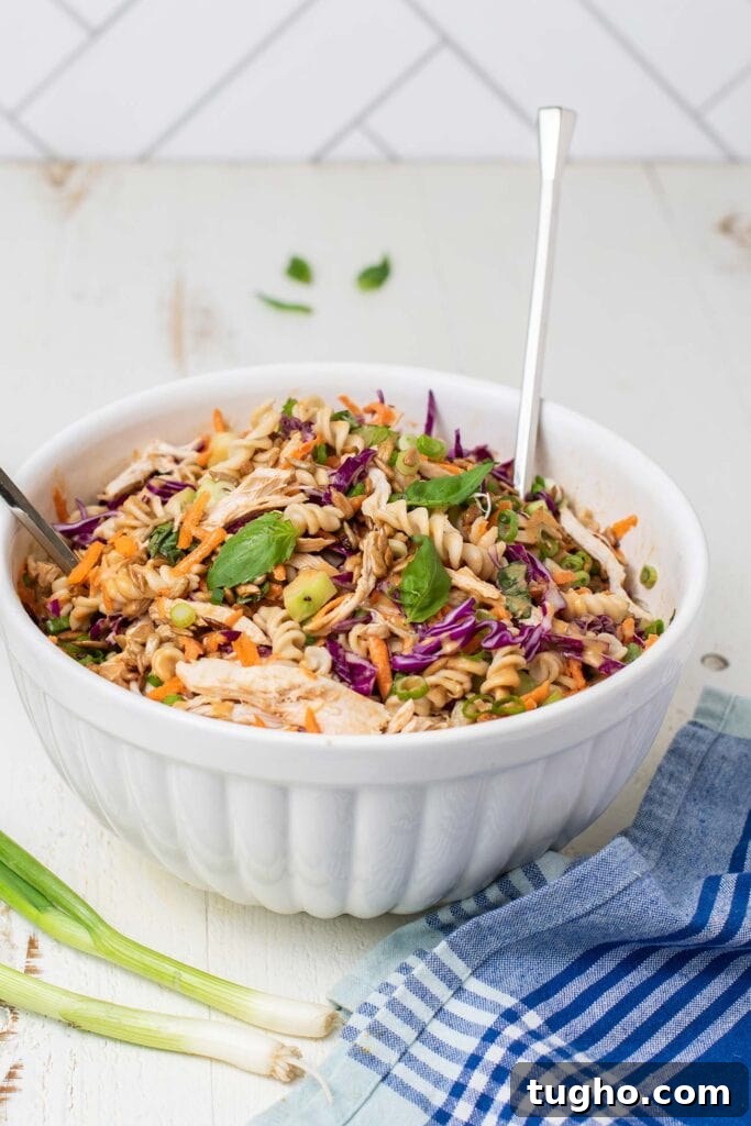 A bowl of pasta salad shown garnished with basil and green onions.