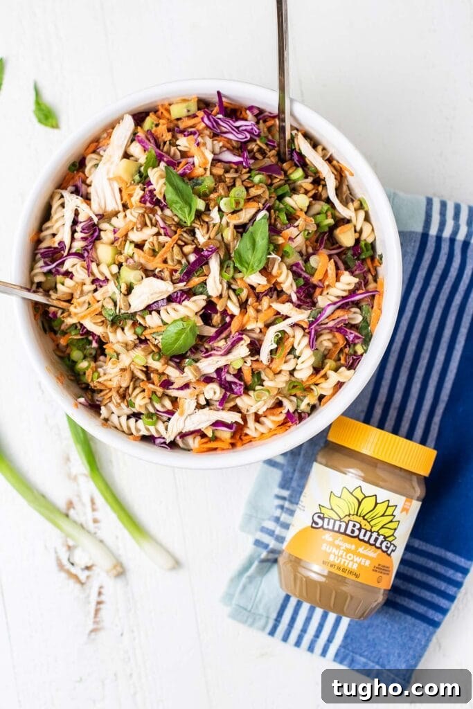 A close up look at a bowl of pasta salad with carrots, purple cabbage, chicken and herbs.