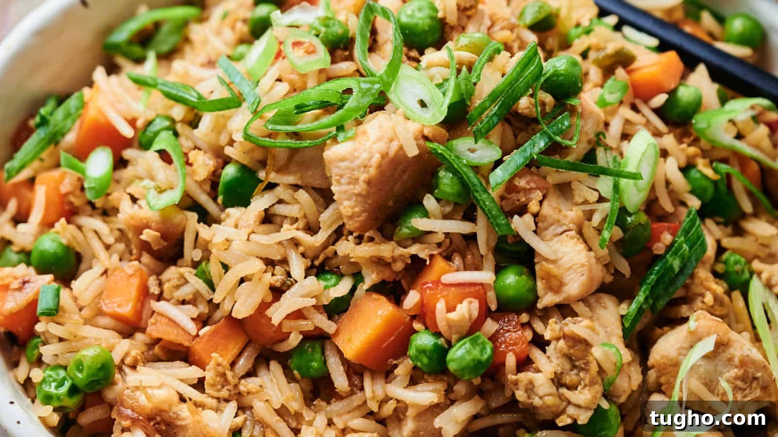 15 Copycat Recipes That Outshine Restaurant Meals 11 Close-up of chicken fried rice with peas, carrots, sliced green onions, and chopsticks.