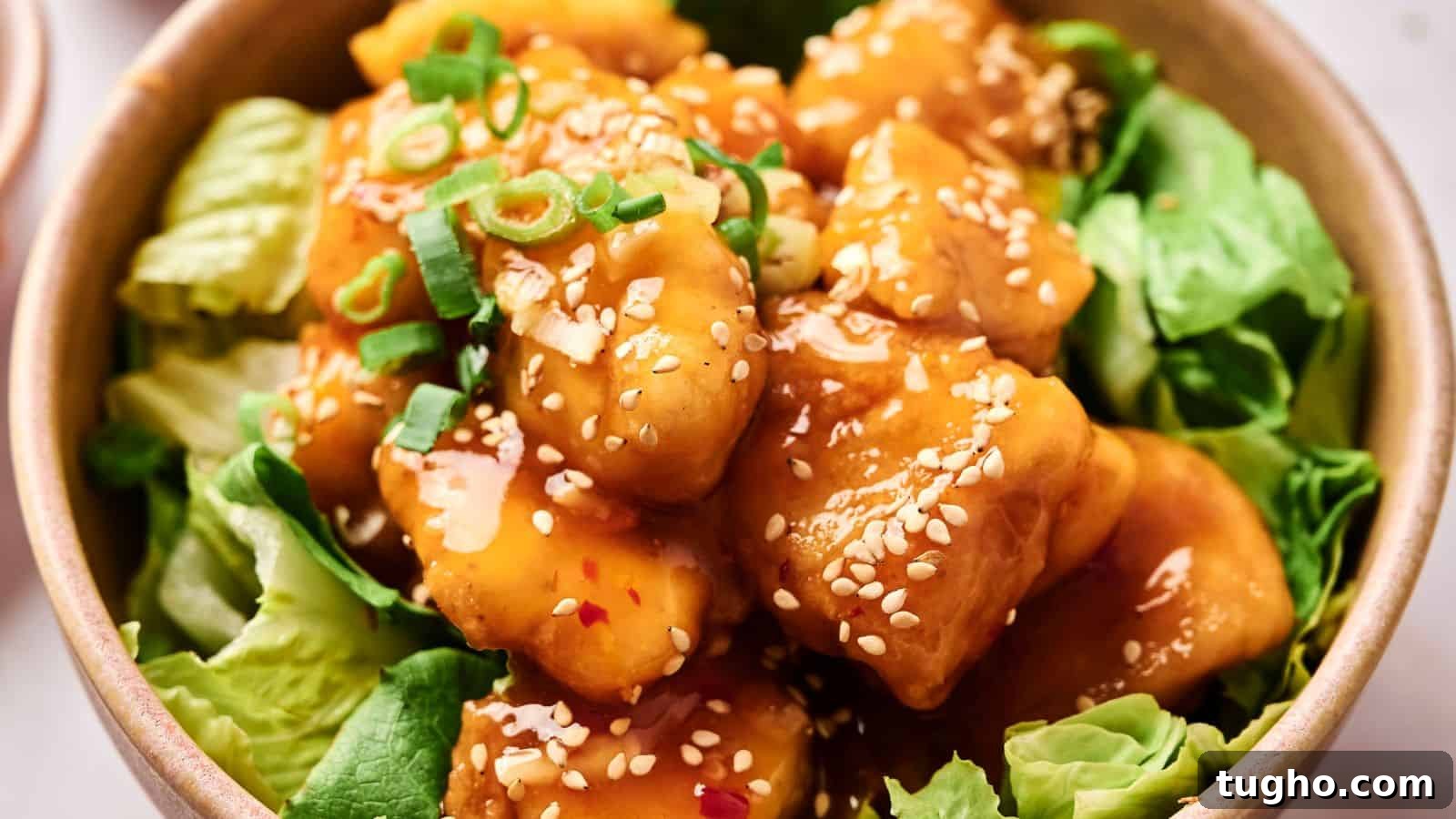 15 Copycat Recipes That Outshine Restaurant Meals 9 A bowl of crispy tofu coated in sesame sauce, garnished with green onions and sesame seeds, served on a bed of lettuce.