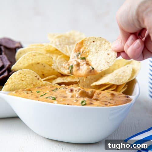 Oven-Baked Sweet and Spicy Chicken Wings Recipe 9 hand dipping a chip into nacho cheese dip in a white bowl.