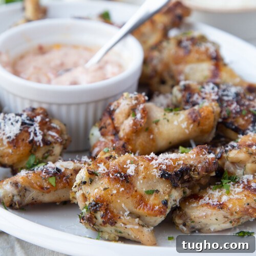 Oven-Baked Sweet and Spicy Chicken Wings Recipe 7 Grilled chicken wings on a white platter with a small bowl of sun dried tomato mayo
