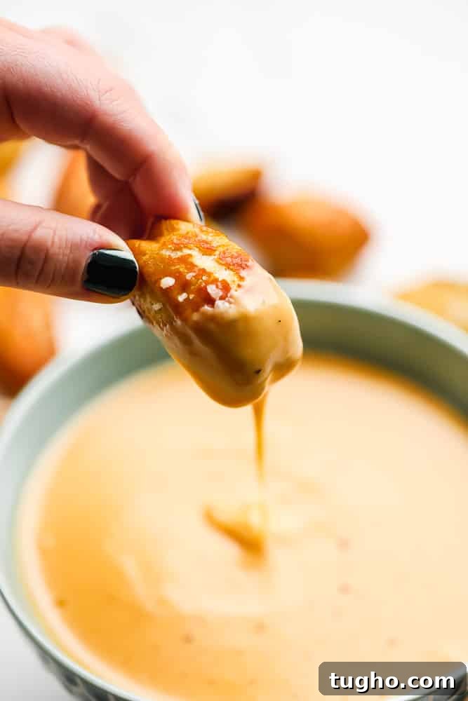 pretzel bite being dipped into cheese sauce, pulled out showing it dripping down into the bowl