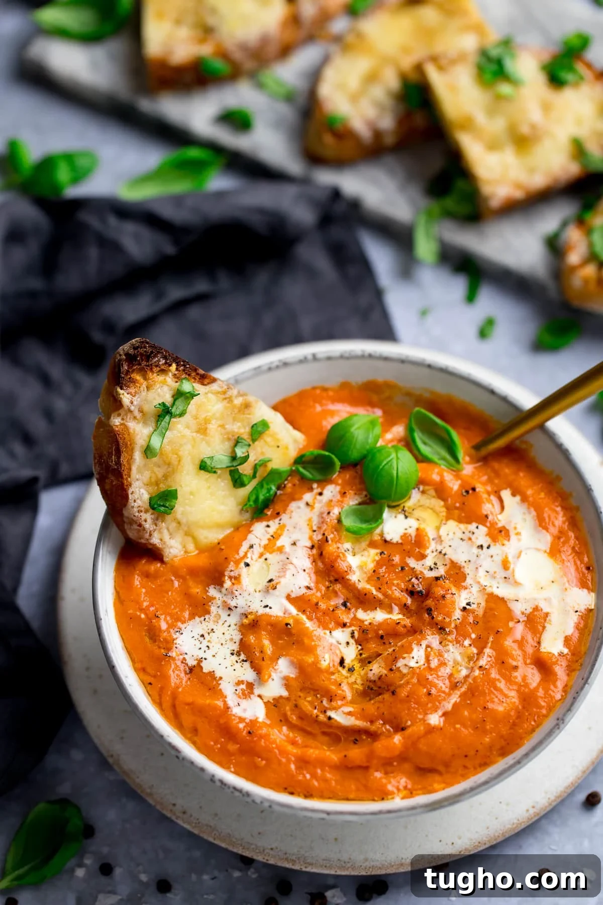 Creamy Homemade Tomato Soup Recipe 2 Bowl of rich tomato soup with a slice of basil-cheese toast in it, and more slices of cheese toast on the side.