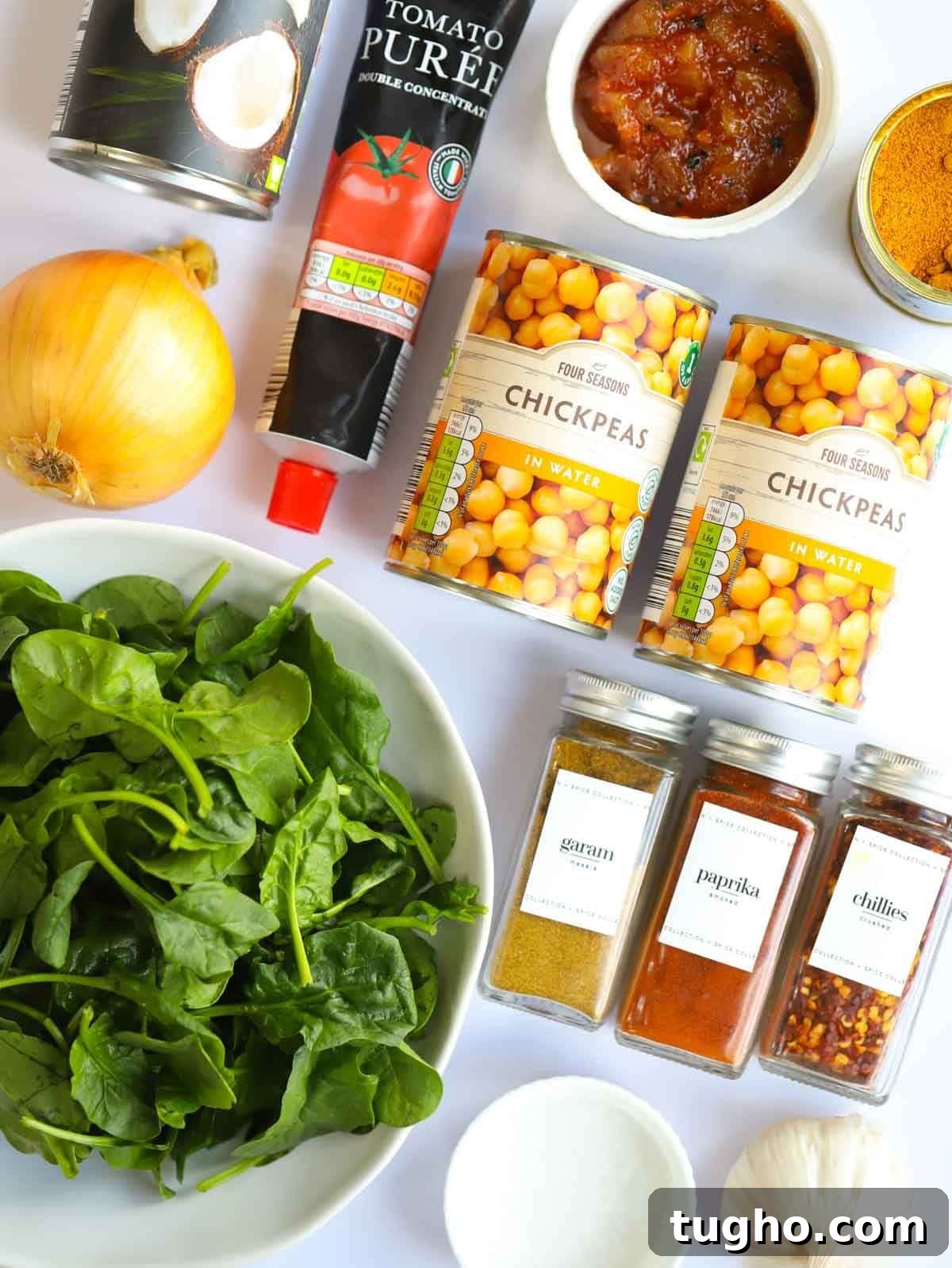 Slow Cooker Chana Saag: Chickpea Curry with Spinach 4 Ingredients including spinach, spices, chickpeas, tomato puree and a lemon laid on a counter.