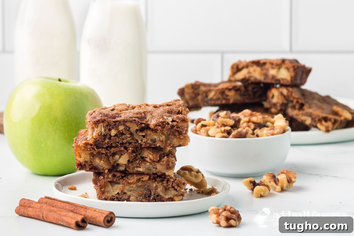 Homemade Apple Walnut Bars Recipe 2 Three Apple Walnut Bars stacked on a white plate with more bars on a plate, a bowl of walnuts, and a green apple in the background.