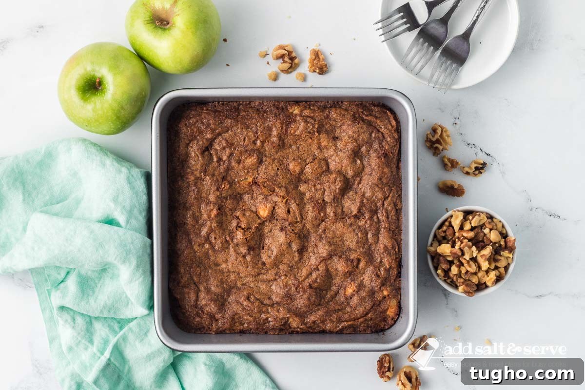 Homemade Apple Walnut Bars Recipe 8 Baked Apple Walnut Bars in an 9-inch by 9-inch pan on a counter surrounded by two green apples, a bowl of walnuts, and a white plate with three forks.