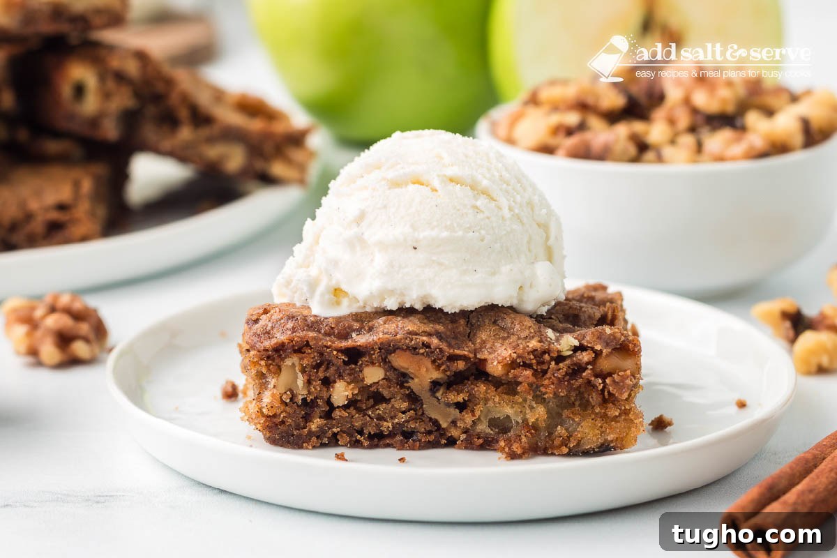 Homemade Apple Walnut Bars Recipe 9 An Apple Walnut Bar topped with vanilla ice cream on a white plate with a green apple and a bowl of walnuts in the background.
