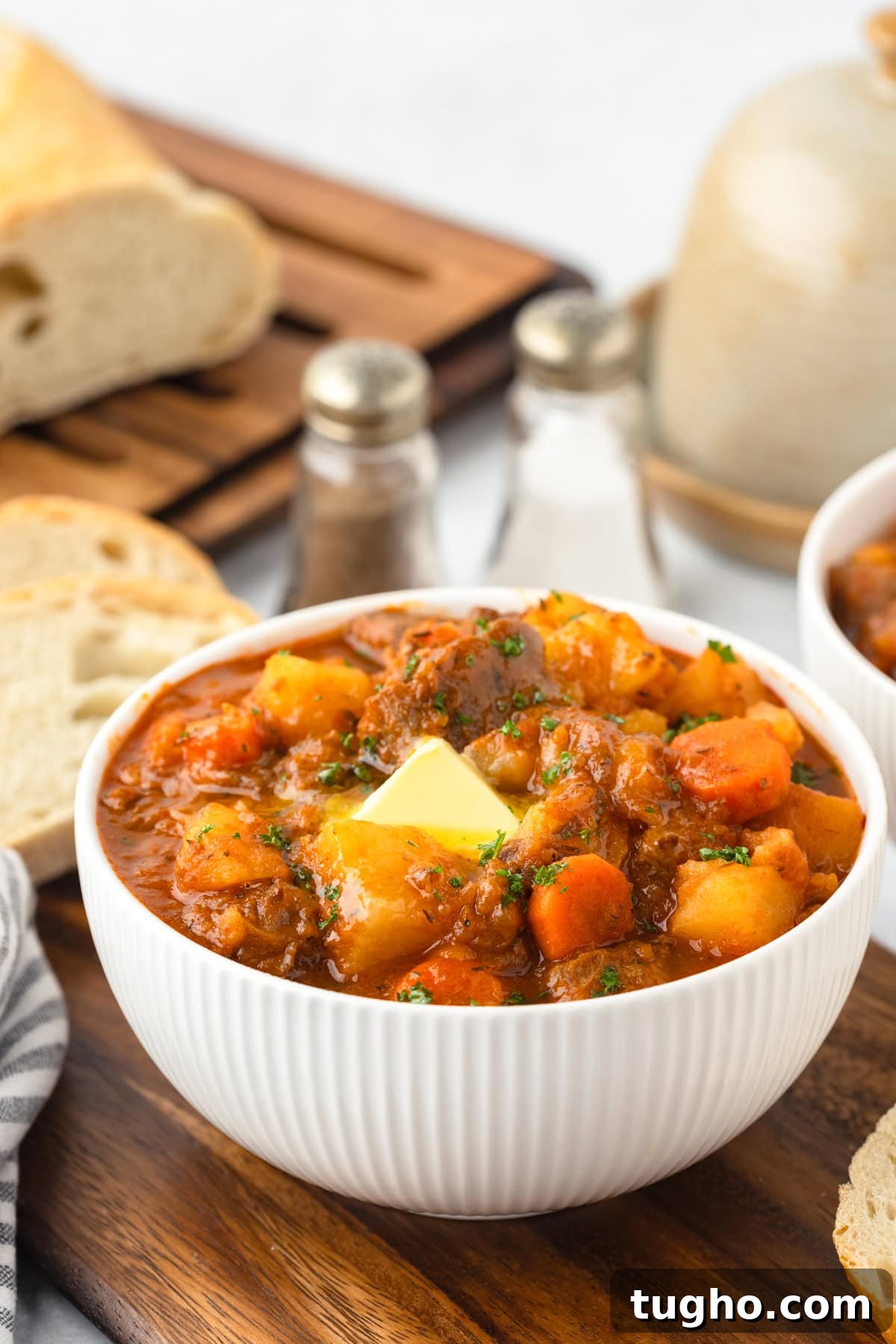 Creamy beef and vegetable stew served in a white bowl with fresh herbs, bread slices in the background, perfect for cozy meals.