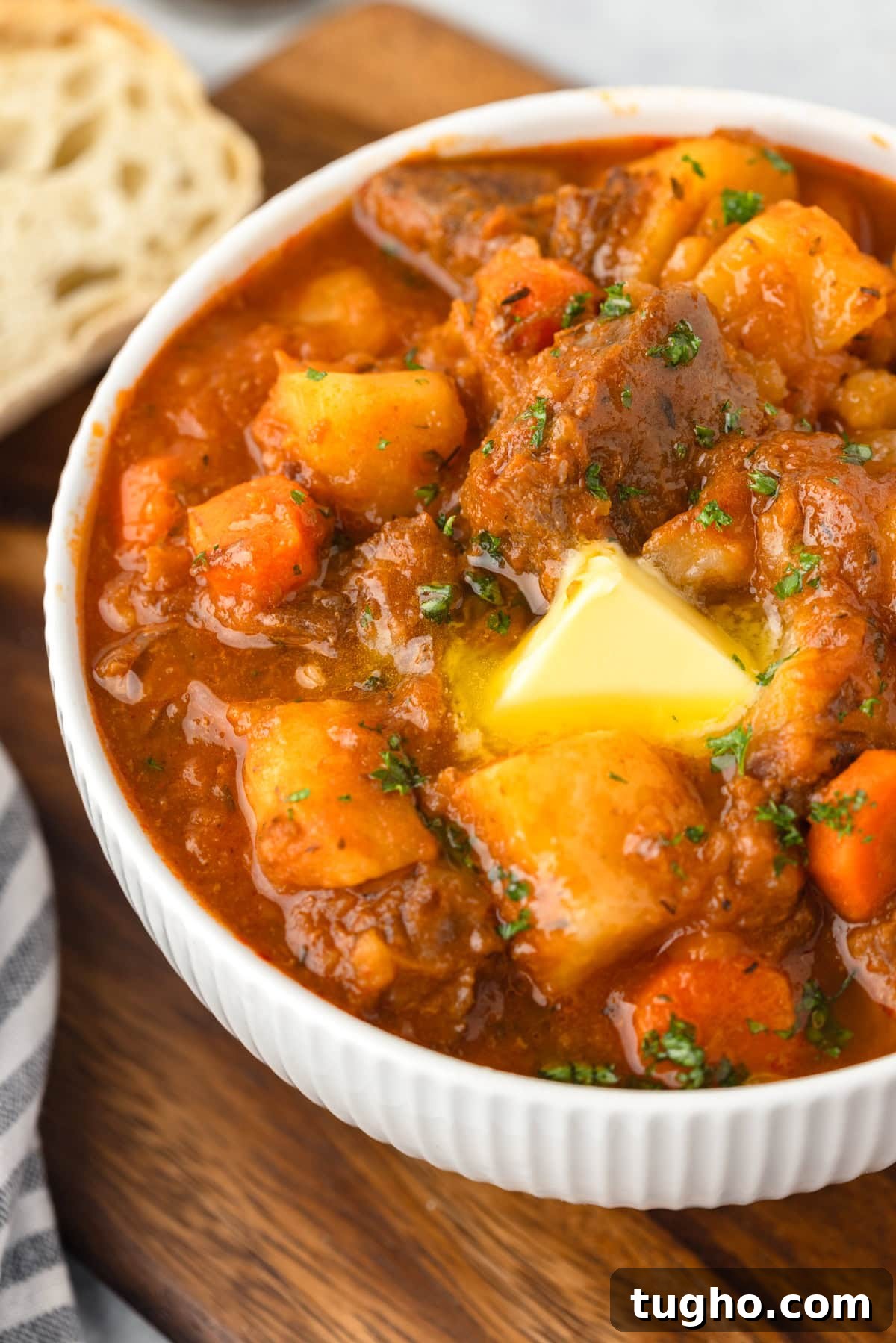 Spicy beef stew with potatoes and vegetables in a white bowl on wooden surface.