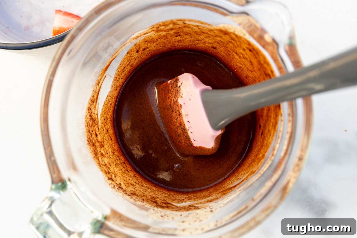 Strawberry Angel Food Cake with Chocolate Sauce 7 Overhead view of a jug of hot chocolate sauce mixture, with a pink spatula in it.