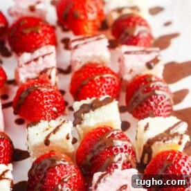 Strawberry Angel Food Cake with Chocolate Sauce 9 Closeup view of strawberries and angel food cake on wooden skewers with chocolate sauce drizzled all over.