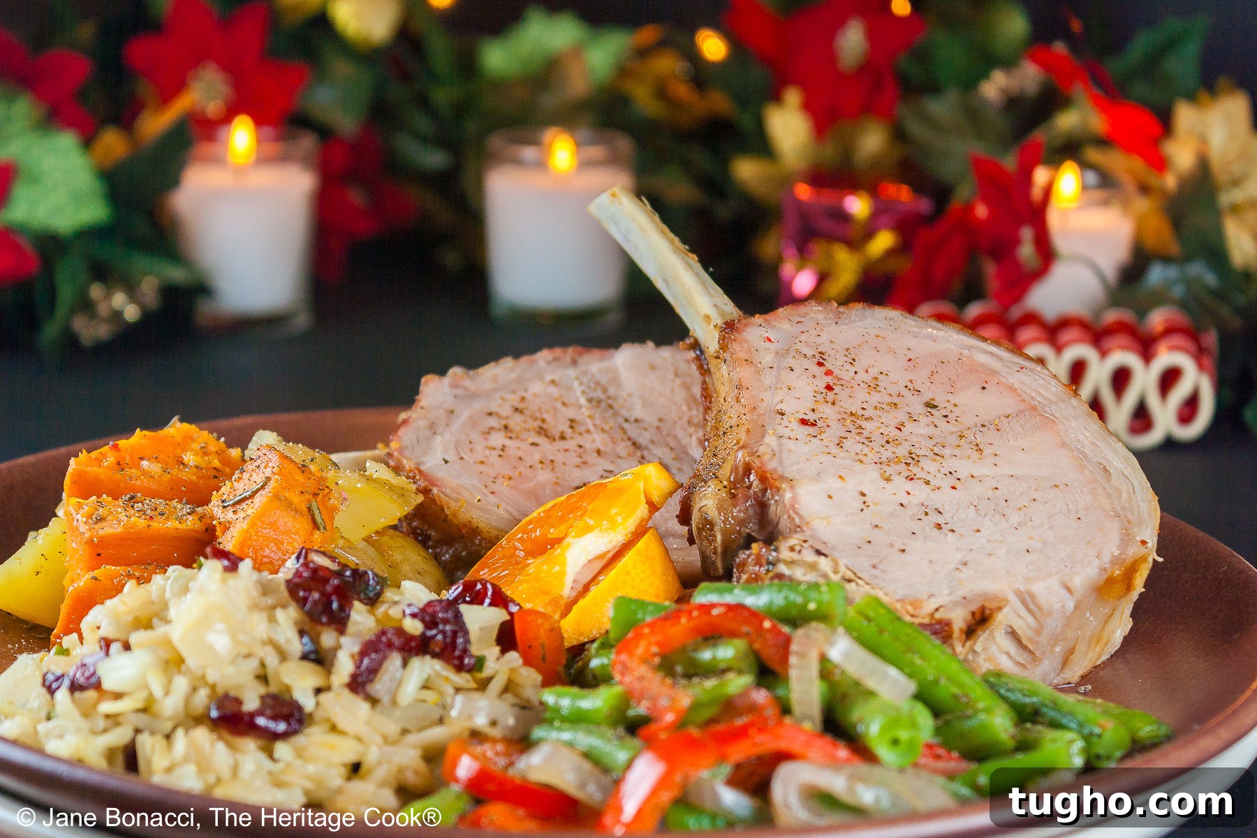 Showstopping Grilled Crown Roast of Pork Recipe 6 Grilled Crown Pork Roast sliced into chops and placed on a dark brown plate with green beans, rice pilaf, and sweet potatoes, surrounded by white candles, green garland with red accents for a festive holiday table © 2024 Jane Bonacci, The Heritage Cook.