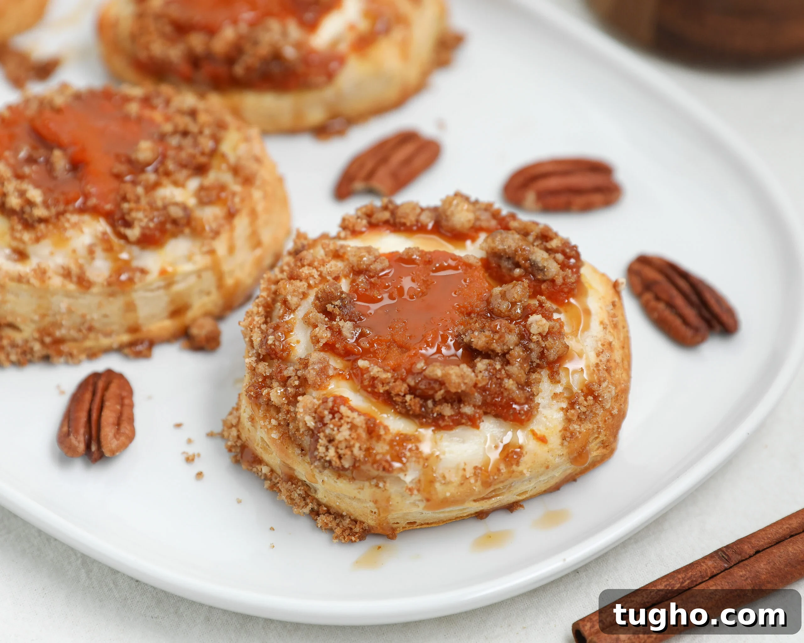 Cinnamon Raisin Bread Pudding Recipe 8 Pumpkin Cream Cheese Danish topped with Biscoff cookie crumble and caramel drizzle on a white plate with pecans and cinnamon sticks.