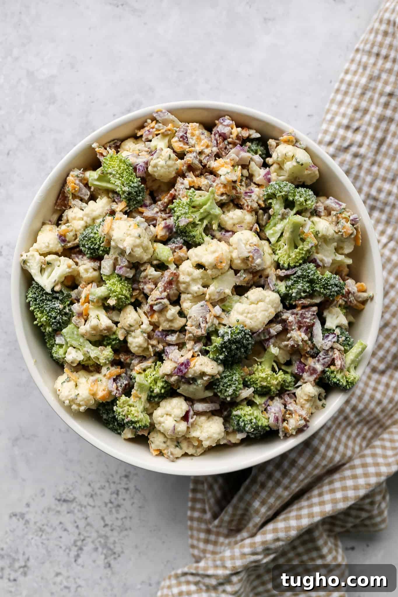 High-Protein Ranch Broccoli and Cauliflower Salad 3 a bowl of high protein ranch broccoli cauliflower salad next to a tan and white gingham kitchen towel