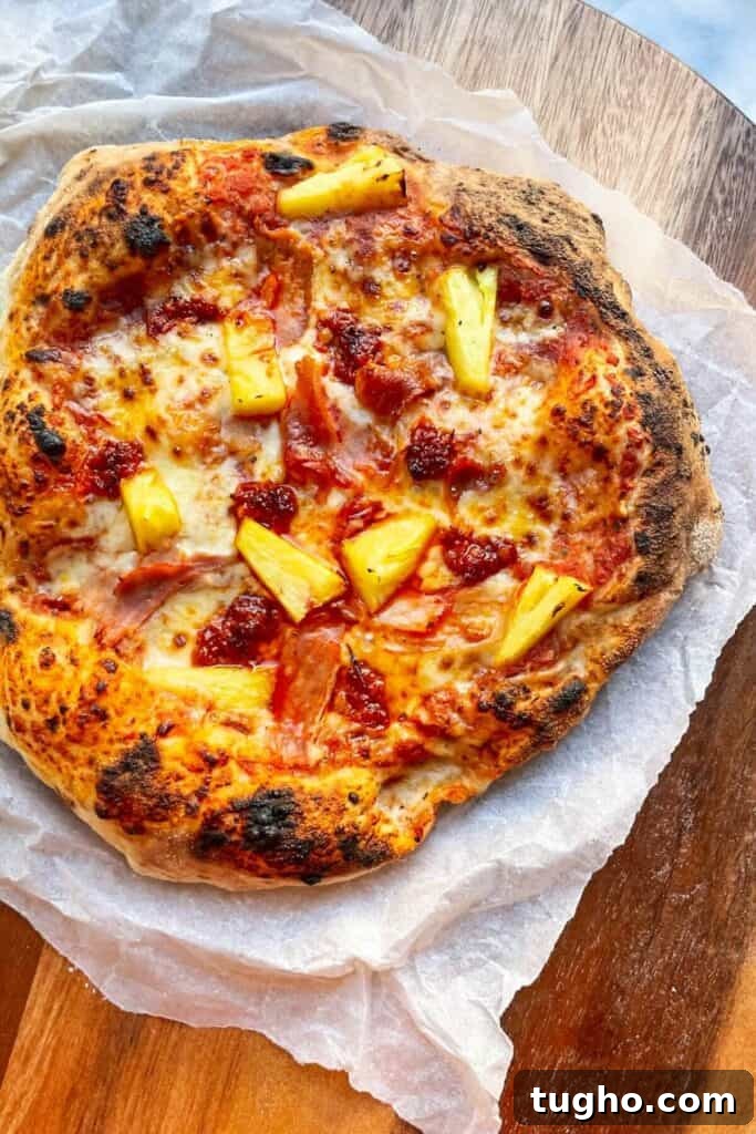 Spicy Hawaiian pizza on baking paper on a round wooden board.