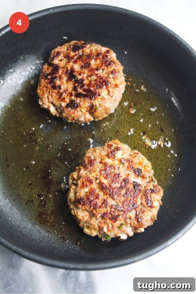 Two lamb patties cooking in a pan.