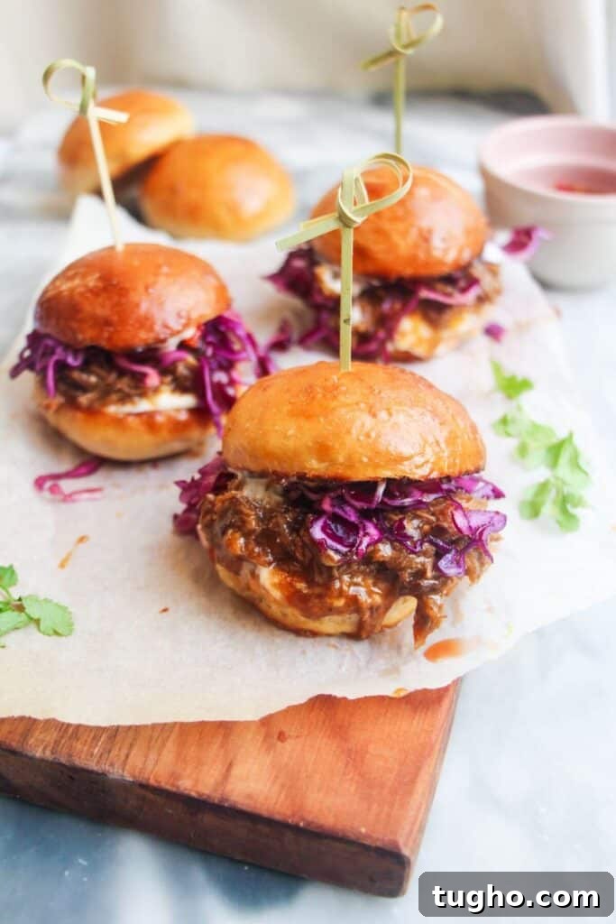 3 pulled pork sliders on a small wooden board.
