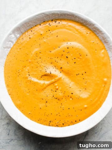 Red pepper cream sauce in a white bowl on a gray surface.