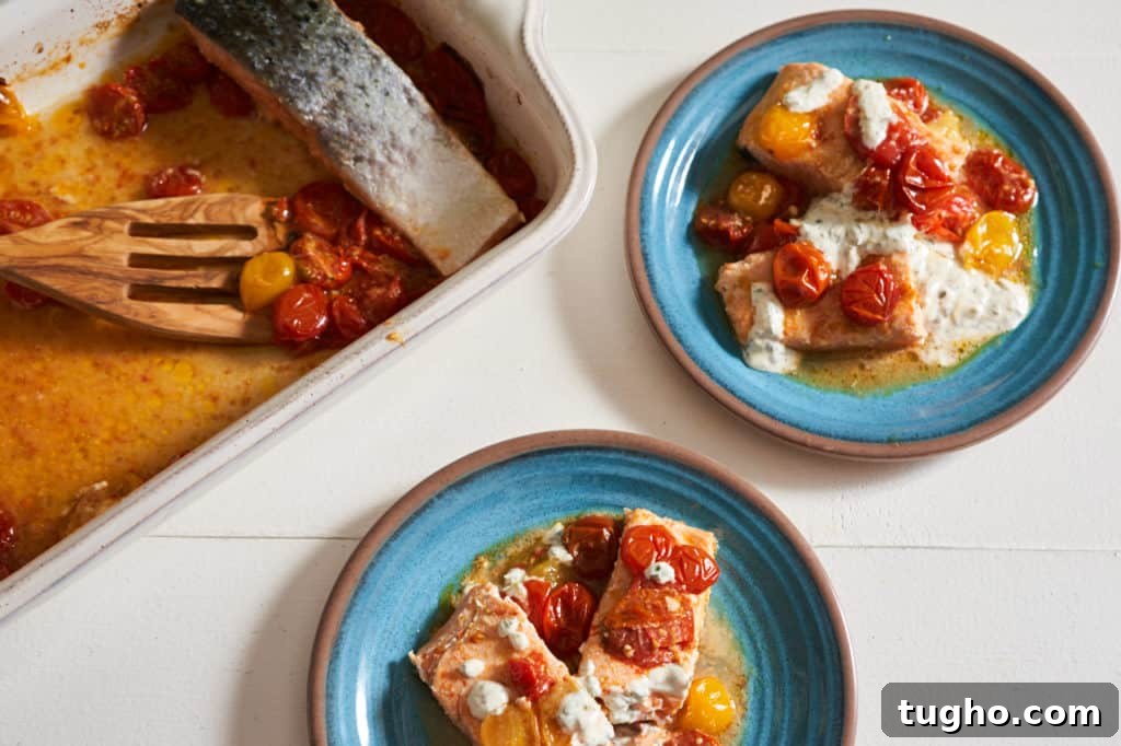 Salmon with roasted tomatoes topped with basil yogurt sauce on a blue plate.