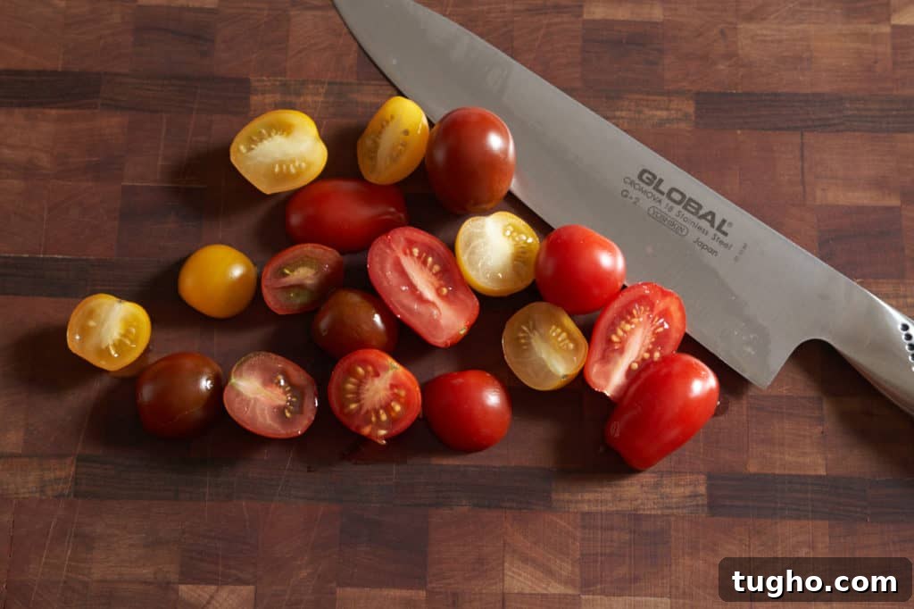 Sliced red and yellow cherry tomatoes on a cutting board with a chef's knife.