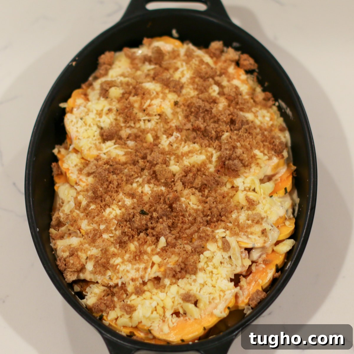 Gruyère and parmesan cheese, along with breadcrumbs, sprinkled over squash in a baking dish.
