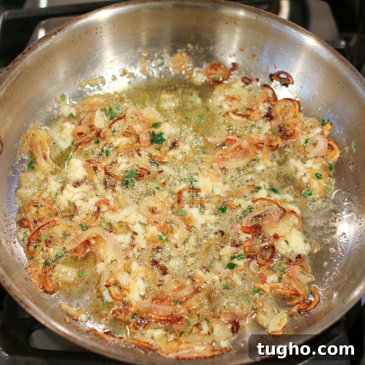 Sautéed garlic and shallots sizzling in butter in a stainless steel pan.