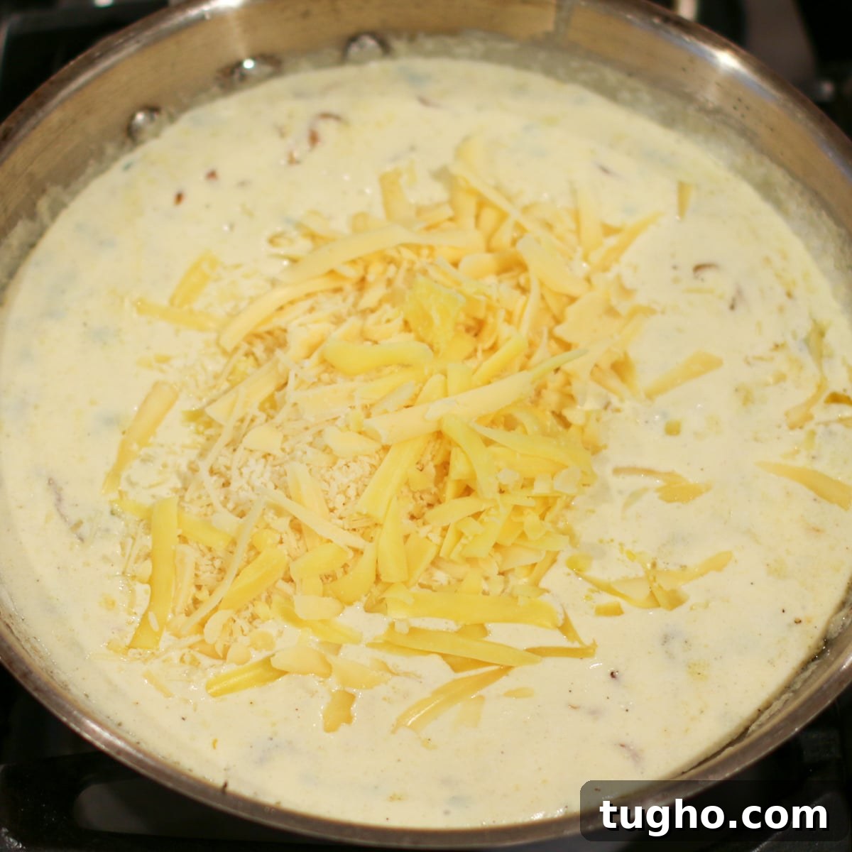 Gruyère and parmesan cheeses being stirred into a pan, melting into a smooth, creamy sauce.