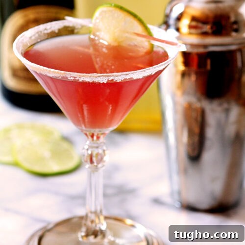Classic Cosmopolitan Cocktail Recipe 8 Cosmopolitan Cocktail on Marble Surface with Cocktail Shaker in Background.
